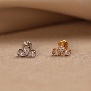 May include: Two stud earrings with flat back posts, one in silver tone and one in gold tone. Each earring features a cluster of three clear, pear-shaped cubic zirconia stones arranged in a fan-like shape, securely set in a metal base.