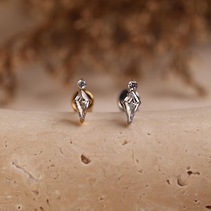 May include: Two stud earrings featuring a kite-shaped clear gemstone topped with a small round clear gemstone. One earring has a gold-toned metal post and backing, while the other earring has a silver-toned metal post and backing.