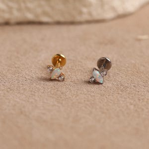 May include: Two stud earrings featuring a central marquise-cut opal stone flanked by two small clear round stones. One earring has a gold-tone metal post and setting, while the other has a dark gunmetal-tone metal post and setting.