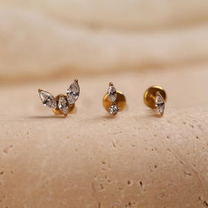 May include: Three gold-tone stud earrings featuring clear marquise and round-cut cubic zirconia stones. The first earring has a cluster of three marquise stones, the second has one marquise and one round stone, and the third has a single marquise stone.