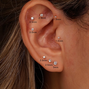 May include: A set of eight small, round, clear stud earrings inserted into various parts of an ear. The studs are labeled with their specific sizes in millimeters, ranging from 1.5mm to 3mm, indicating the diameter of each individual gemstone.
