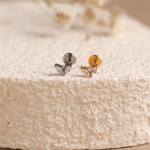 May include: Two flat-back stud earrings featuring a leaf-shaped design with two marquise-cut clear stones. One earring is silver-toned and the other is gold-toned, both showcasing a delicate botanical aesthetic with a secure circular backing.