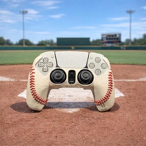 May include: A baseball-themed video game controller, featuring a cream-colored design with red stitching, resembling a baseball. The controller has black buttons and a white faceplate, set against a baseball field background.