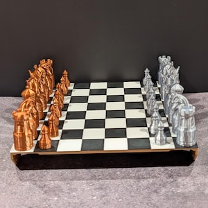 May include: A complete chess set with a black and white checkered board. The chess pieces are in two colors: bronze and silver. The pieces are arranged on the board, ready for a game.