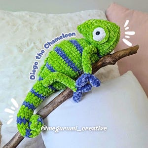 Può includere: Un camaleonte all'uncinetto verde e blu fatto a mano chiamato "Diego" appollaiato su un ramo di legno. Il peluche ha un occhio bianco ed è realizzato con filato morbido e strutturato. Il testo "Diego the Chameleon" è scritto sul lato.