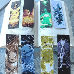 May include: A collection of six rectangular bookmarks featuring various Pokémon characters. The bookmarks are inserted into an open book. Each bookmark displays a different character in vibrant colors, with detailed illustrations and artistic backgrounds.