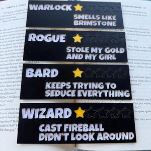 Könnte beinhalten: Vier schwarze Lesezeichen mit weißem Text und gelben Sternakzenten. Die Lesezeichen lauten "Warlock Smells Like Brimstone", "Rogue Stole My Gold and My Girl", "Bard Keeps Trying to Seduce Everything" und "Wizard Cast Fireball Didn't Look Around".