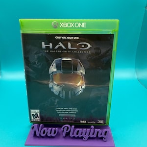 May include: A Halo: The Master Chief Collection video game case for Xbox One. The case features a helmet graphic and the text "Now Playing" on a purple stand. The game is rated M for Mature.