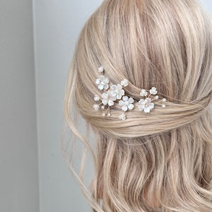May include: A set of three gold hair clips with white pearl flowers. The clips are arranged in a cluster and are perfect for adding a touch of elegance to any hairstyle.
