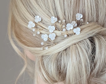 Op de afbeelding: Een set van drie gouden haar kammen met witte parel-achtige bloemen en kleine parel accenten. De kammen zijn gerangschikt in een bloemmotief.