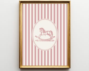 May include: A framed print featuring a pink and white striped background. An oval in the center contains a pink illustration of a rocking horse. The frame is gold.
