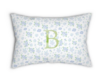 Può includere: Cuscino rettangolare con sfondo bianco ricoperto da piccoli motivi floreali blu. Una grande lettera "B" verde è centrata sul cuscino. Articolo decorativo.