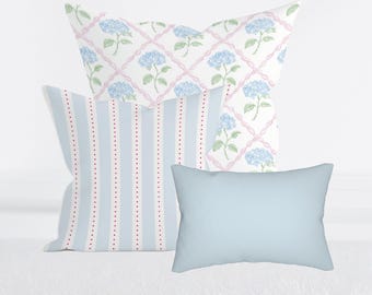 May include: Three decorative cushions. One has a light blue and white striped pattern with red dots. Another features a hydrangea floral design on a white background. The third cushion is a solid light blue.
