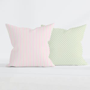 May include: Two square throw pillows. The left pillow features a vertical striped pattern in light pink and sage green. The right pillow displays a small-scale sage green and white gingham check pattern. Both pillows have a soft, plush appearance.