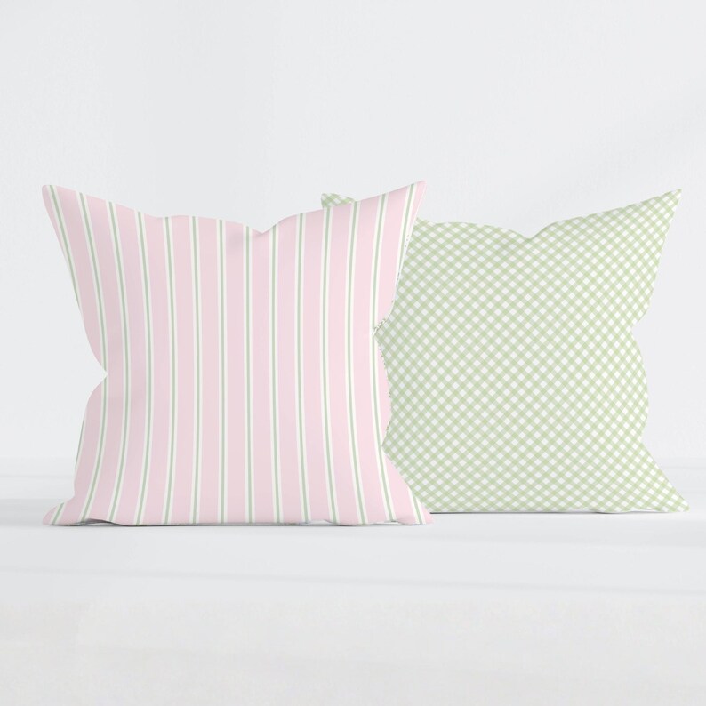May include: Two square throw pillows. The left pillow features a vertical striped pattern in light pink and sage green. The right pillow displays a small-scale sage green and white gingham check pattern. Both pillows have a soft, plush appearance.