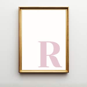 Pode incluir: Uma impress&atilde;o de arte de parede retangular com uma letra R mai&uacute;scula grande em rosa p&aacute;lido centralizada no quadrante inferior direito. A impress&atilde;o est&aacute; emoldurada numa moldura fina de metal dourado com uma borda branca ao redor.