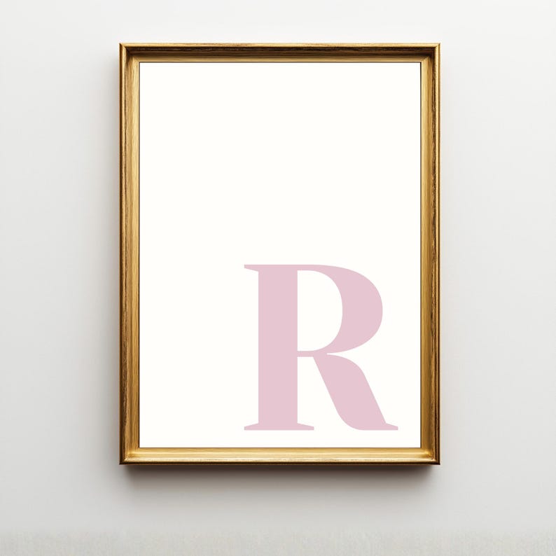 Pode incluir: Uma impress&atilde;o de arte de parede retangular com uma letra R mai&uacute;scula grande em rosa p&aacute;lido centralizada no quadrante inferior direito. A impress&atilde;o est&aacute; emoldurada numa moldura fina de metal dourado com uma borda branca ao redor.