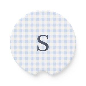 May include: A round car coaster with a light blue and white gingham pattern. The coaster features the letter "S" in a dark blue color. The coaster has a small notch for easy removal from a car cup holder.