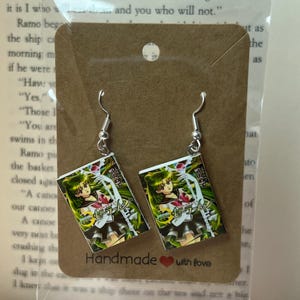 May include: A pair of silver-toned dangle earrings. Each earring features a rectangular charm with a colorful anime illustration and Japanese text. The earrings are displayed on a brown card that reads "Handmade with love."