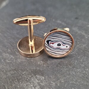 Può includere: Un paio di gemelli in oro con un'intarsio di pietra di agata rotonda, nera, bianca e rossa.