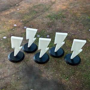 May include: Six white lightning bolt shaped tokens on black bases. The tokens are arranged in a row.