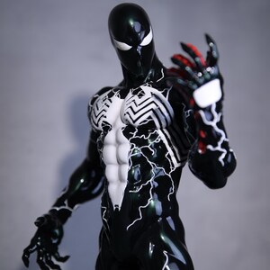 May include: A glossy black superhero action figure with white detailing and a white spider emblem on the chest. The figure has red and black hands and a white mask with white eyes. The figure is posed with one arm raised.