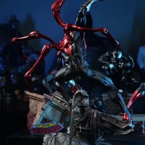 May include: A dynamic statue of a superhero in a black and red suit, posed mid-action. The figure is atop a detailed base with the words "AMAZING SPIDER-MAN". Red metallic appendages extend from the figure's back.