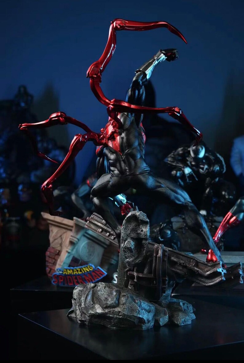 May include: A dynamic statue of a superhero in a black and red suit, posed mid-action. The figure is atop a detailed base with the words "AMAZING SPIDER-MAN". Red metallic appendages extend from the figure's back.