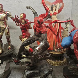May include: A collection of superhero figurines, including Iron Man and Spider-Man, in dynamic poses. The Spider-Man figure is in a crouching position with red and black detailing. Other figures are in red and gold armor.