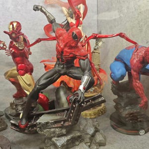 May include: A collection of superhero figurines, including Spider-Man in a dynamic pose with red and black suit, and Iron Man in a red and gold suit. Other figures include a woman in a red outfit and another Spider-Man figure.