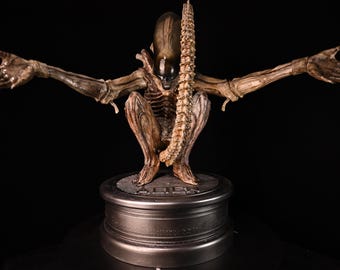 Alien statue model classic pose — crouching, with base, painted in biomechanical colors.