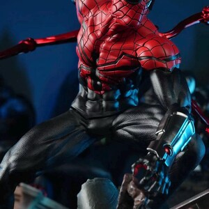 May include: A detailed action figure of Spider-Man in a dynamic pose. The figure features a red and black costume with intricate web detailing. The figure has multiple articulated arms and is set against a dark blue background.