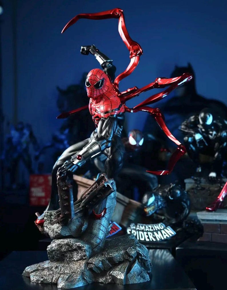 May include: A detailed action figure of Spider-Man in a dynamic pose, featuring a red and black suit with metallic red spider-arms. The figure is set on a rocky base with the words "Amazing Spider-Man" visible. Other superhero figures are in the background.