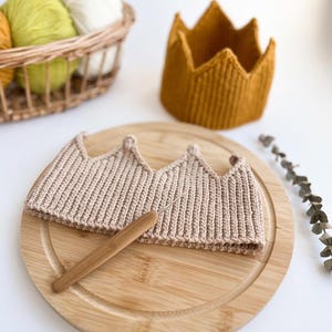 May include: A beige crocheted crown with a wooden crochet hook on a wooden chopping board.