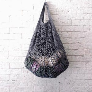 Può includere: Una borsa di rete grigia a maglia appesa a un muro di mattoni bianchi. La borsa è piena di oggetti rotondi bianchi.