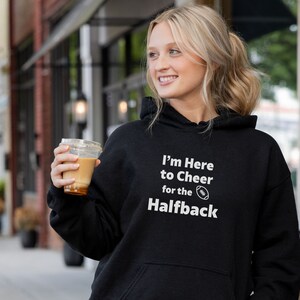 Puede incluir: Sudadera con capucha negra con texto blanco que dice "Estoy aquí para animar al corredor" con un icono de fútbol.