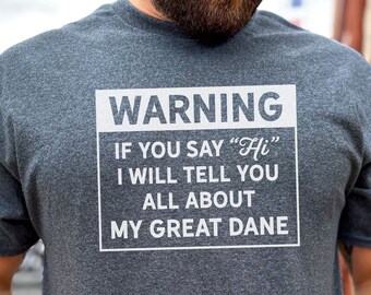 May include: A dark gray t-shirt with a white warning sign that reads "WARNING IF YOU SAY "Hi" I WILL TELL YOU ALL ABOUT MY GREAT DANE."