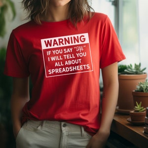 Op de afbeelding: Rood T-shirt met een wit waarschuwingsbord met de tekst "WARNING IF YOU SAY "Hi" I WILL TELL YOU ALL ABOUT SPREADSHEETS"