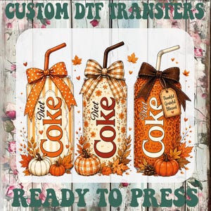 May include: A graphic design featuring three Diet Coke cans with straws, decorated with bows, autumn leaves, and pumpkins. The text reads CUSTOM DTF TRANSFERS READY TO PRESS, Thankful, Grateful, Blessed. The cans have orange stripes, floral, and leopard patterns.