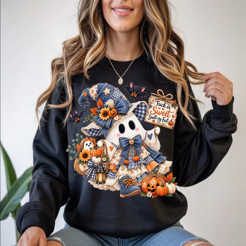 May include: A black crewneck sweatshirt featuring a graphic of a ghost wearing a blue plaid witch hat and dress. The ghost holds a sign that reads Trick or Sweet Smell my Feet, surrounded by sunflowers, pumpkins, a lantern, and small bats.