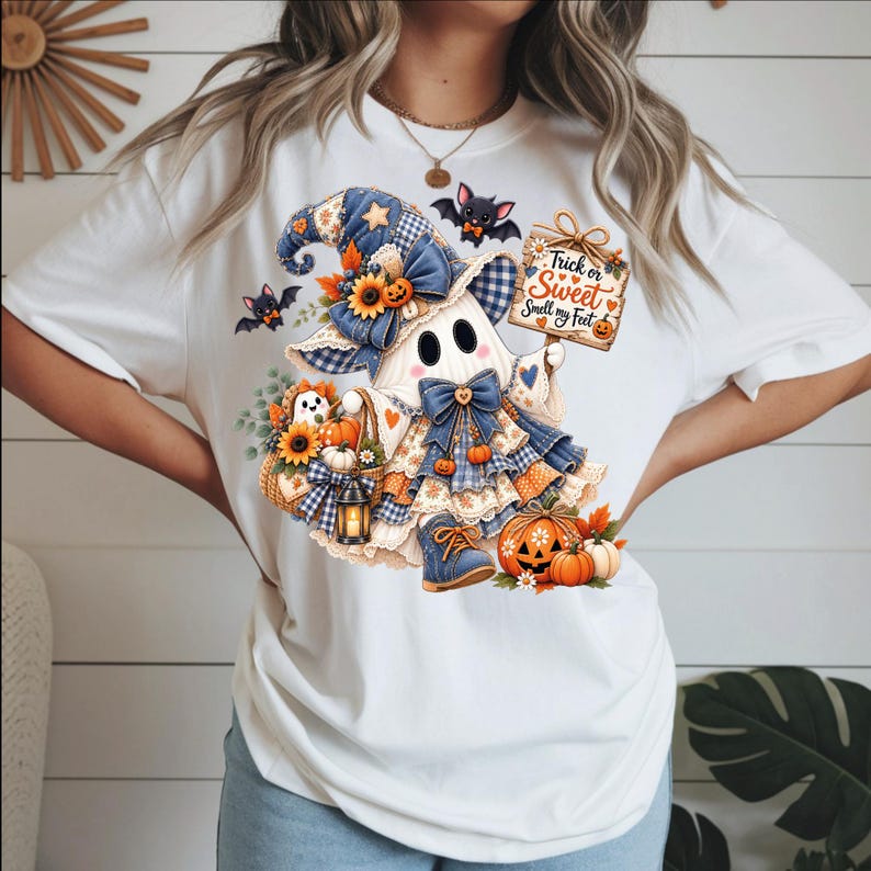 May include: A white t-shirt featuring a graphic of a ghost wearing a blue plaid hat and dress, holding a sign that reads Trick or Sweet Smell my Feet. The design includes sunflowers, pumpkins, bats, and a lantern, rendered in blue and orange tones.