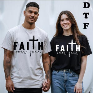 Peut inclure: Un t-shirt beige clair avec le texte noir FAITH OVER FEAR et une croix, et un t-shirt noir avec le texte blanc FAITH OVER FEAR et une croix. Les lettres DTF sont imprimées dans le coin supérieur droit de l'image.