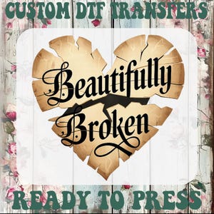 May include: A distressed heart design with the words "Beautifully Broken" in black script. The heart is a parchment color with cracks, set against a floral and wood-grain background. Text at the top reads "CUSTOM DTF TRANSFERS" and at the bottom "READY TO PRESS".