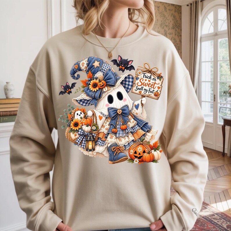 May include: A beige crewneck sweatshirt featuring a graphic of a ghost wearing a blue plaid witch hat and dress, holding a sign that reads Trick or Sweet Smell my Feet. The design includes sunflowers, pumpkins, bats, and a lantern.