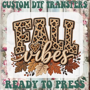 May include: A custom DTF transfer featuring the text FALL VIBES in a leopard print pattern with a small leopard print heart. The design includes a cluster of autumn leaves in shades of brown, orange, and tan, with the text READY TO PRESS below.