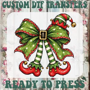 May include: A graphic design featuring a large green polka-dot bow with a gold buckle, topped with a red and green elf hat with a bell. Two striped green and white elf legs extend downward into curled red elf shoes with gold bells. Text reads CUSTOM DTF TRANSFERS READY TO PRESS.
