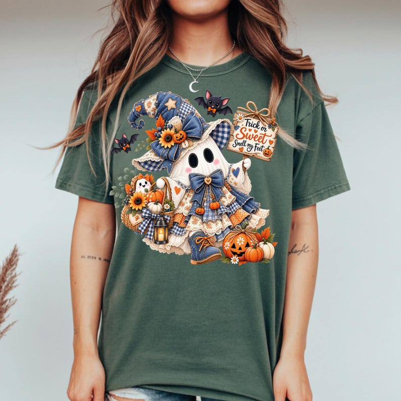 May include: A dark green t-shirt featuring a graphic of a ghost wearing a blue plaid hat and bow, holding a basket with sunflowers and pumpkins. The design includes small bats, a lantern, and a sign that reads Trick or Sweet Smell my Feet.