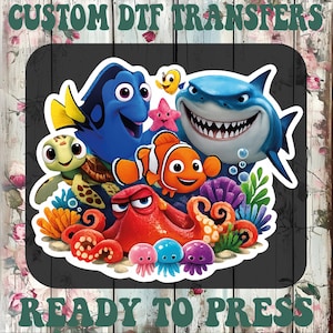 May include: A colorful DTF transfer featuring characters from the movie "Finding Nemo." The design includes Dory, Nemo, Bruce the shark, and other sea creatures. The text "CUSTOM DTF TRANSFERS" and "READY TO PRESS" are at the top and bottom.