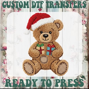May include: A brown teddy bear wearing a Santa hat, holding two wrapped gifts. The bear has a stitched design with a patch on its belly. The text "CUSTOM DTF TRANSFERS" and "READY TO PRESS" are at the top and bottom of the image.