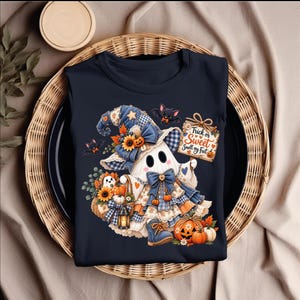 May include: A dark navy t-shirt featuring a graphic of a ghost wearing a blue plaid witch hat and dress, holding a sign that reads Trick or Sweet Smell my Feet. The design includes sunflowers, pumpkins, bats, and a lantern in orange, blue, and white.